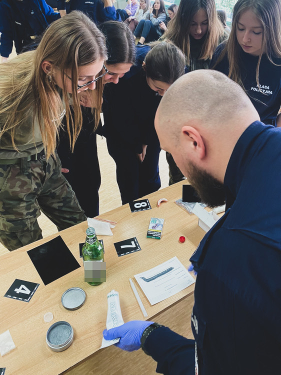 Policjant podczas zajęć z techniki kryminalistycznej prezentuje zabezpieczenia śladów daktyloskopijnych.