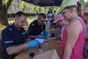 Policjanci wykonują dzieciom odbitki linii papilarnych.