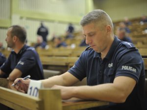 Uczestnicy konkursu Policjant Ruchu Drogowego podczas pisania testu sprawdzającego umiejętności w zakresie udzielania pomocy ofiarom wypadków komunikacyjnych. Aula Centrum Szkolenia Policji.