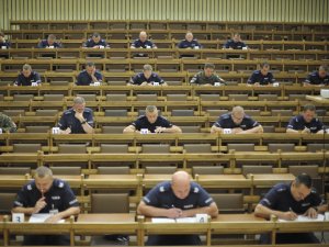 Uczestnicy konkursu Policjant Ruchu Drogowego podczas pisania testu sprawdzającego umiejętności w zakresie udzielania pomocy ofiarom wypadków komunikacyjnych. Aula Centrum Szkolenia Policji.