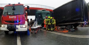 Na zdjęciu znajdują się po prawej stronie pojazdy uczestniczące w zdarzeniu po lewej  wóz strażacki, pośrodku strażacy uczestniczący w akcji ratunkowej