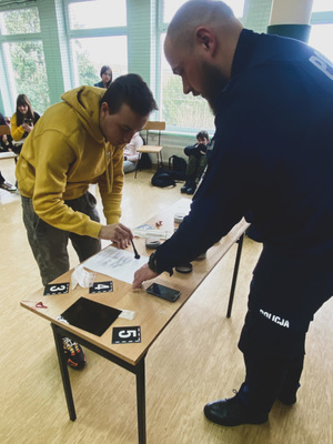 Policjant podczas zajęć z techniki kryminalistycznej prezentuje zabezpieczenia śladów daktyloskopijnych.